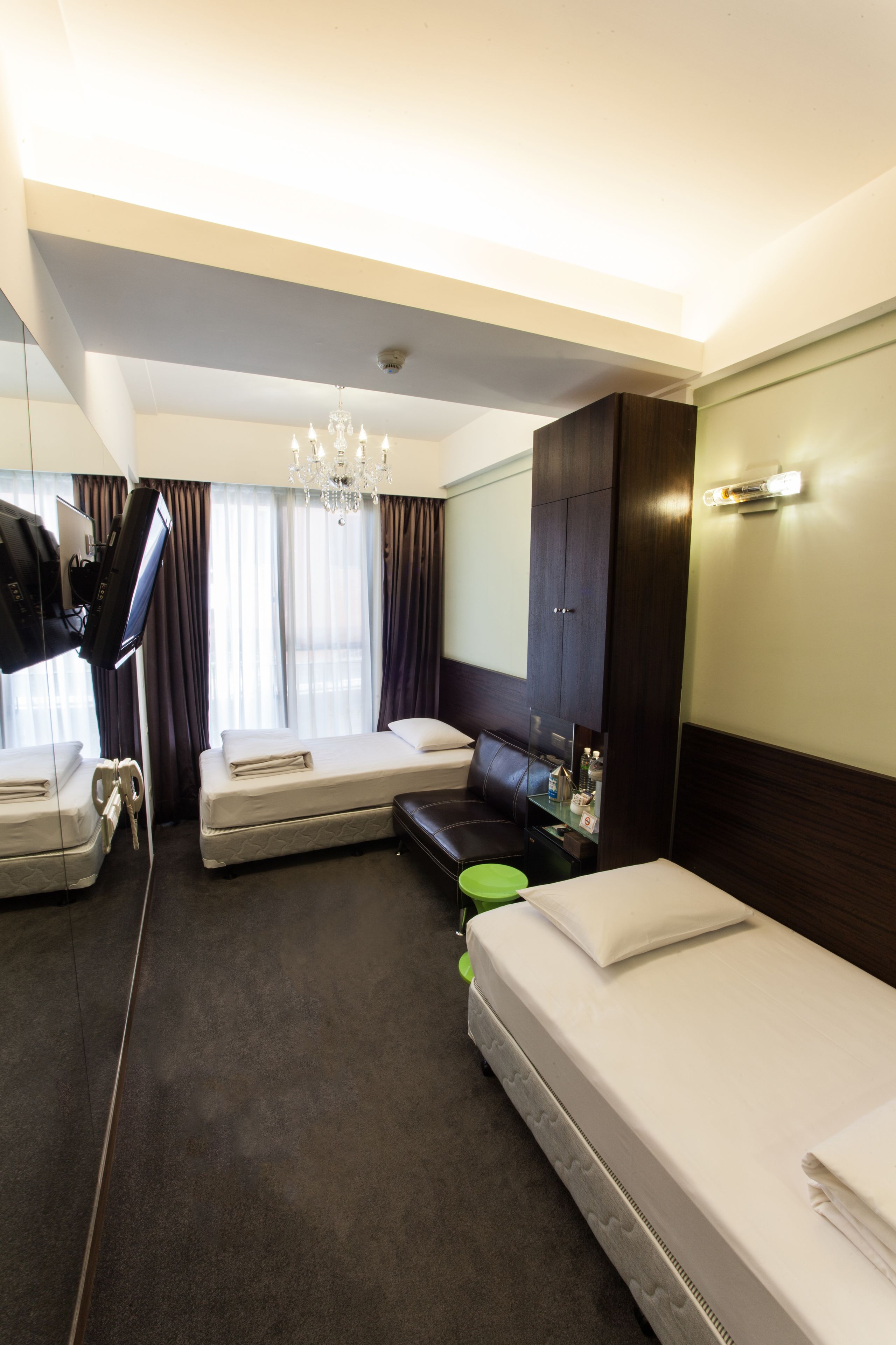 A hotel room with two beds, a television, a desk, a mirror, and a chandelier.