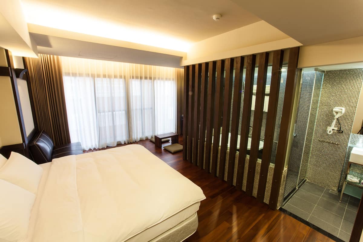 Habitación de hotel con una cama grande, un escritorio, una silla, cabina de ducha de vidrio y vistas al exterior.