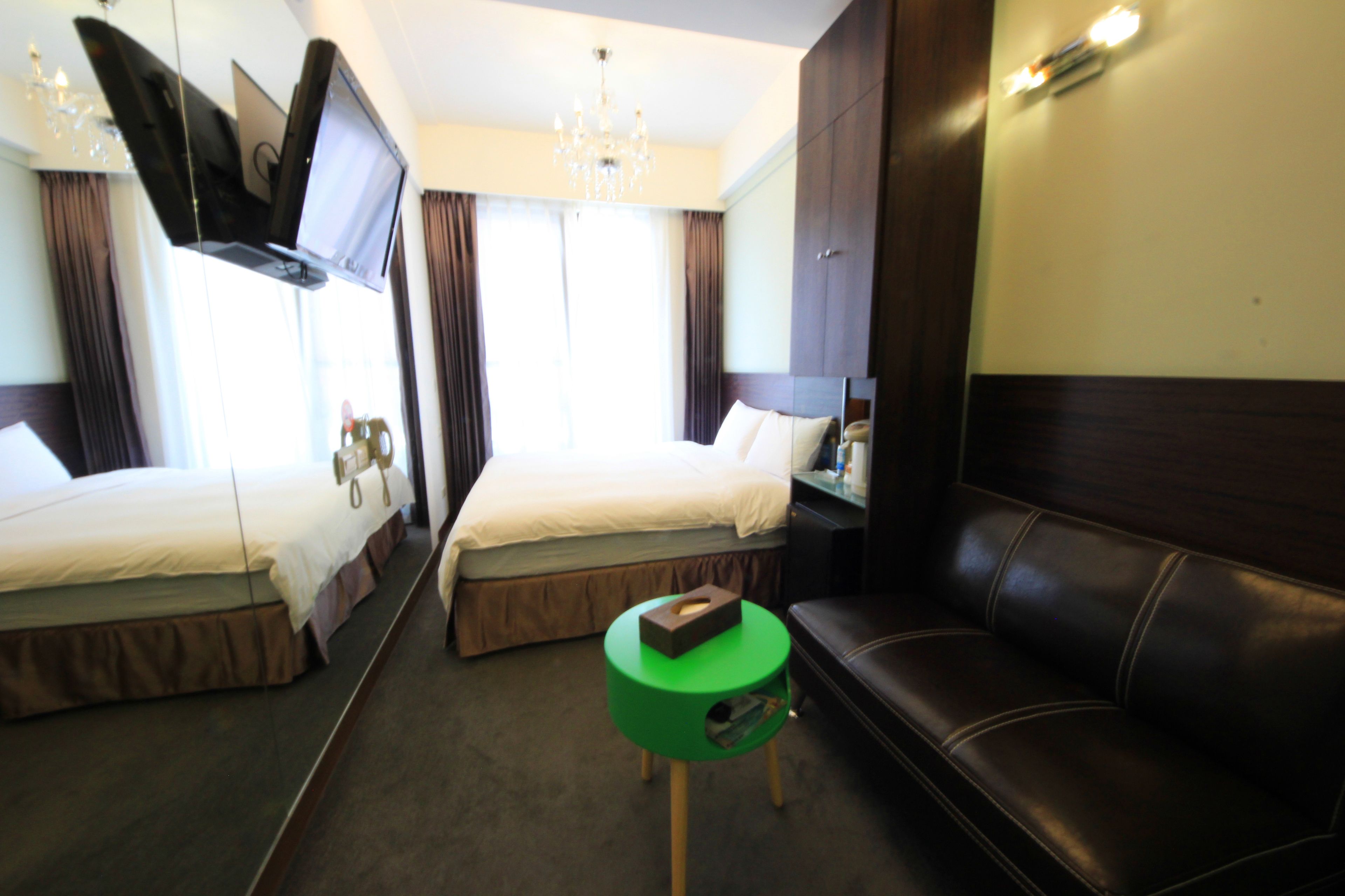 Camera d'albergo con due letti, un tavolino verde, una poltrona in pelle, una TV a schermo piatto fissata al muro e un lampadario.