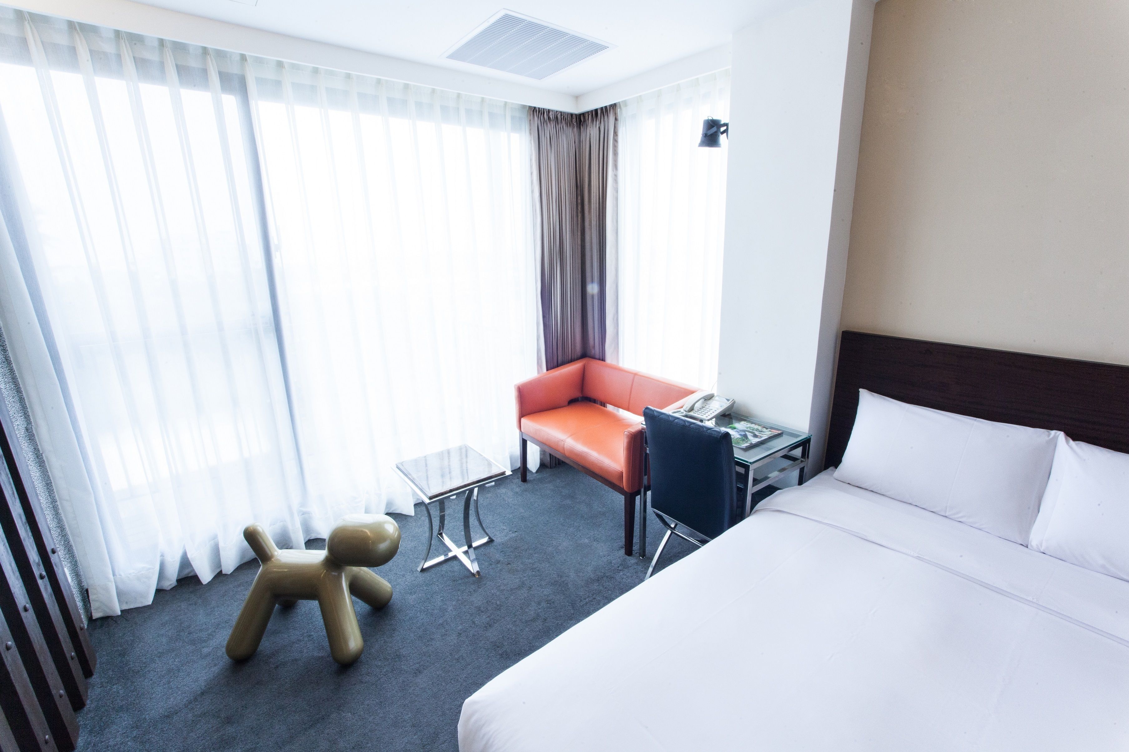 Una habitación de hotel con una cama, un escritorio, una silla, una mesita pequeña y un oso de peluche.
