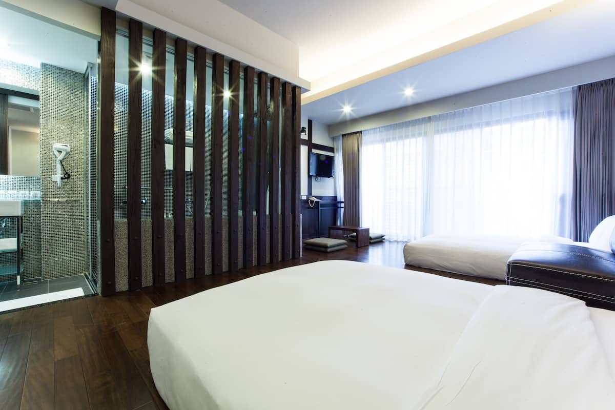 Una habitación de hotel con una cama grande, zona de ducha, televisión y ventana con cortinas.