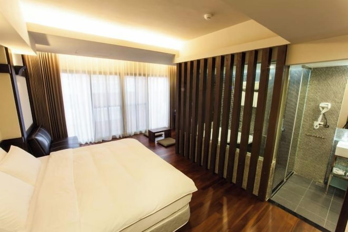 Habitación de hotel con una cama grande, cabina de ducha de vidrio y vistas al exterior.