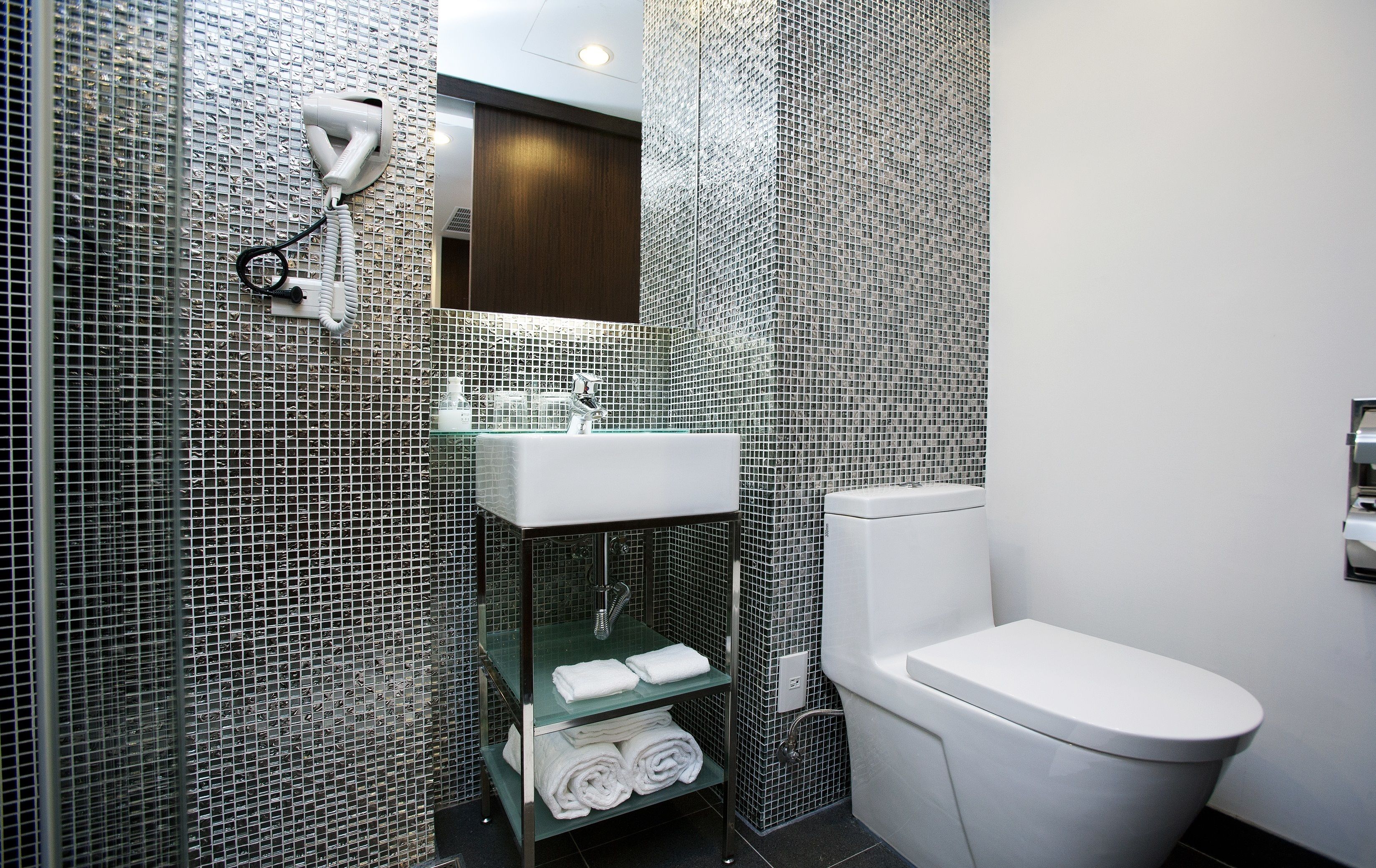 A bathroom with a tiled wall, a sink, a mirror, a towel rack, and a toilet.