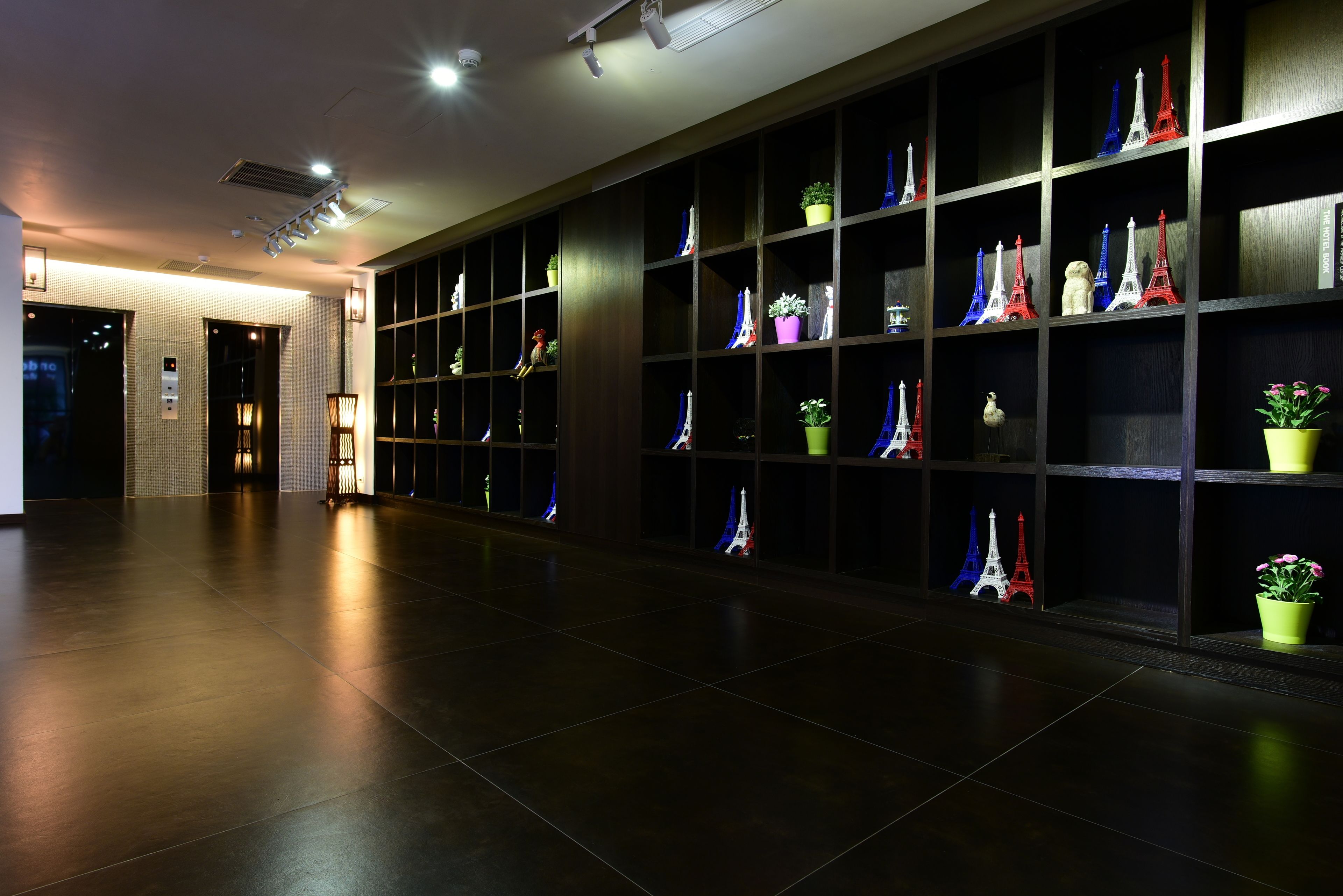 A hallway with dark wooden shelves displaying Eiffel Tower models and potted plants.