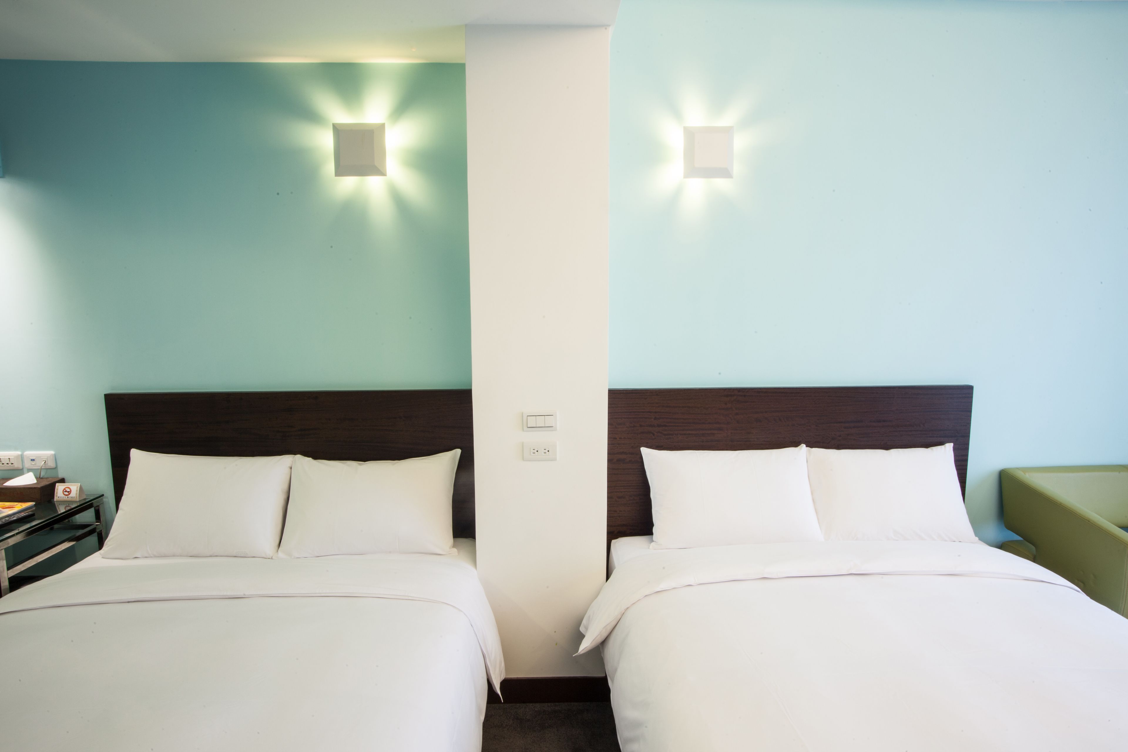 A hotel room with two beds, a nightstand, and wall-mounted lights.