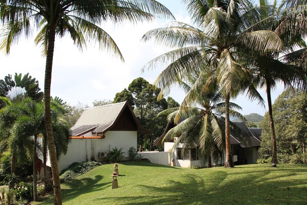 A traditional house with a sloped roof, surrounded by lush greenery and palm trees.