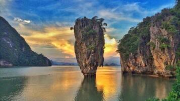 A natural rock formation in a calm body of water with surrounding greenery and a clear sky.