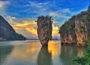 A natural rock formation in a calm body of water with surrounding greenery and a clear sky.