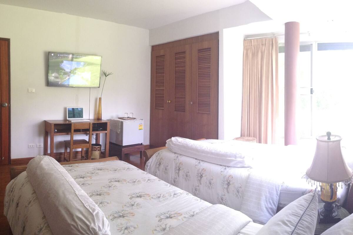 Une chambre avec deux lits, un bureau, une télévision et une fenêtre avec des rideaux.