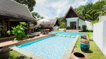 A swimming pool with lounge chairs and a covered seating area, surrounded by tropical vegetation and a clear sky.