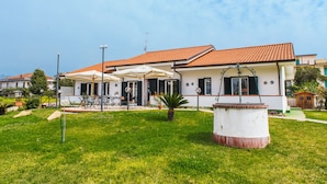 A two-story house with a tiled roof, a covered patio with outdoor furniture, and a well-maintained lawn. - Hotel Villa Maredona (Ascea)