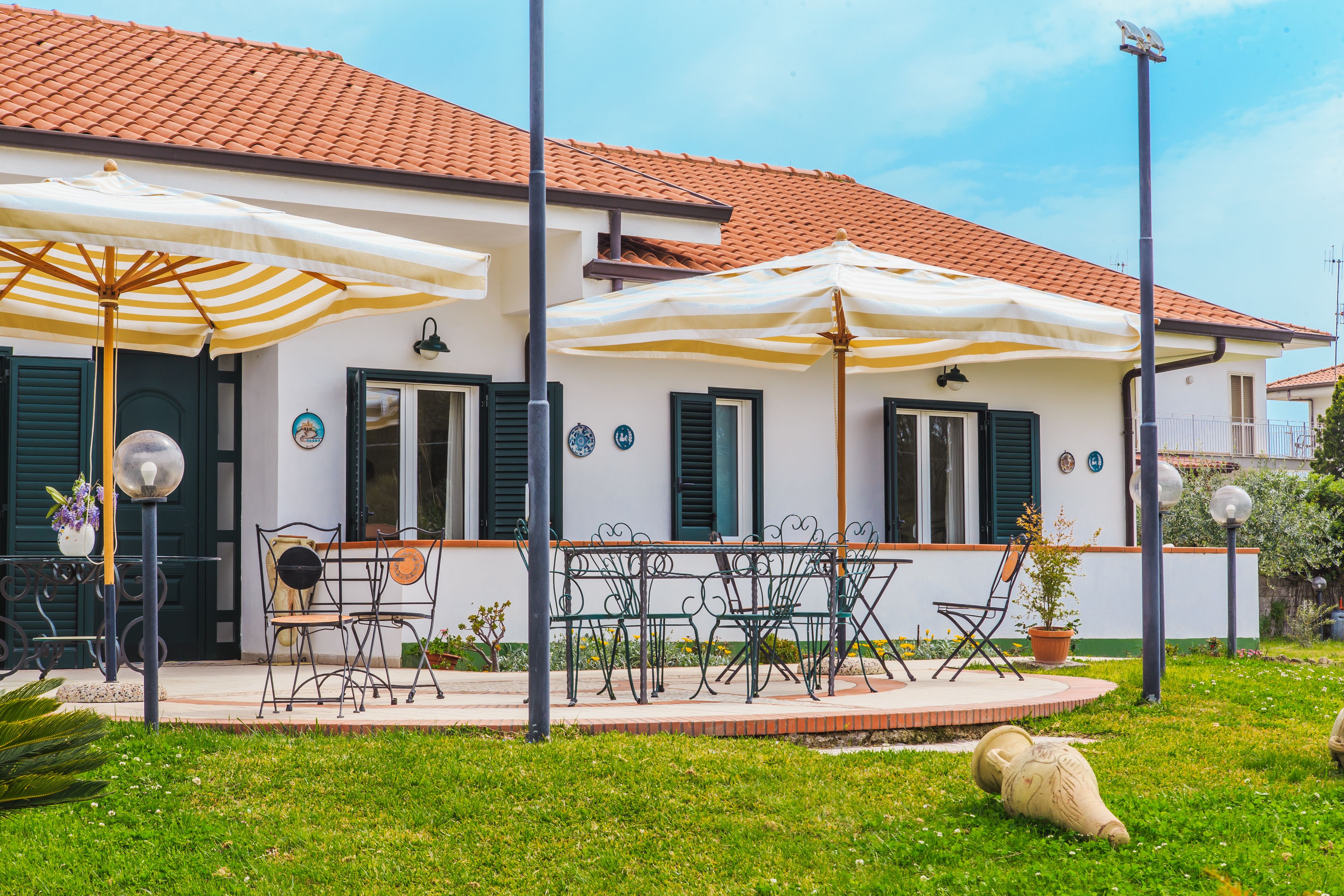 A house with a tiled roof, outdoor seating with umbrellas, and a well-maintained lawn.