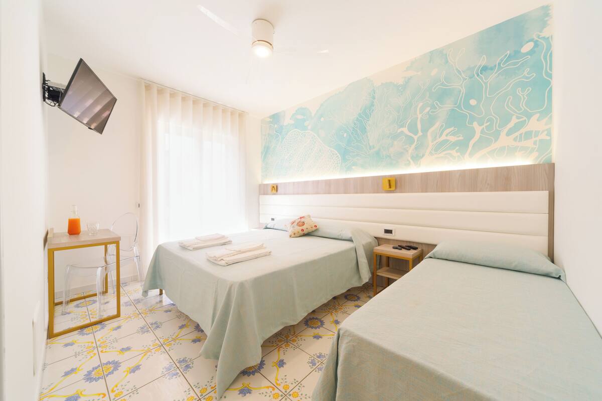 A hotel room with two beds, a TV mounted on the wall, a small table with a chair, and a decorative wall piece.