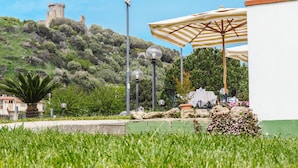 A courtyard with a castle in the background, outdoor seating, and a lamp post. - Hotel Villa Maredona (Ascea)