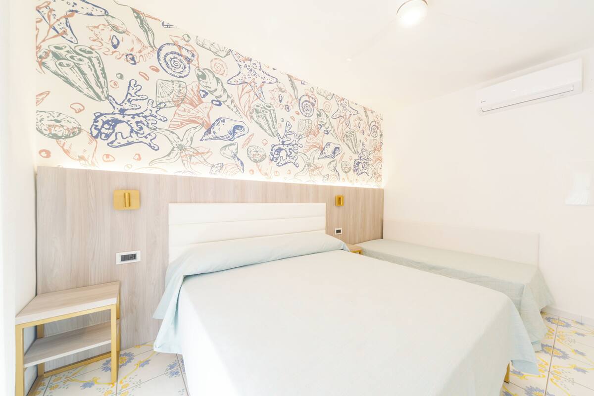 A hotel room with two beds, a wooden headboard, a small table, and a wall mural.