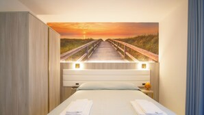 A hotel room with a bed, a nightstand, a lamp, and a painting of a sunset over a boardwalk. - Hotel Villa Maredona (Ascea)