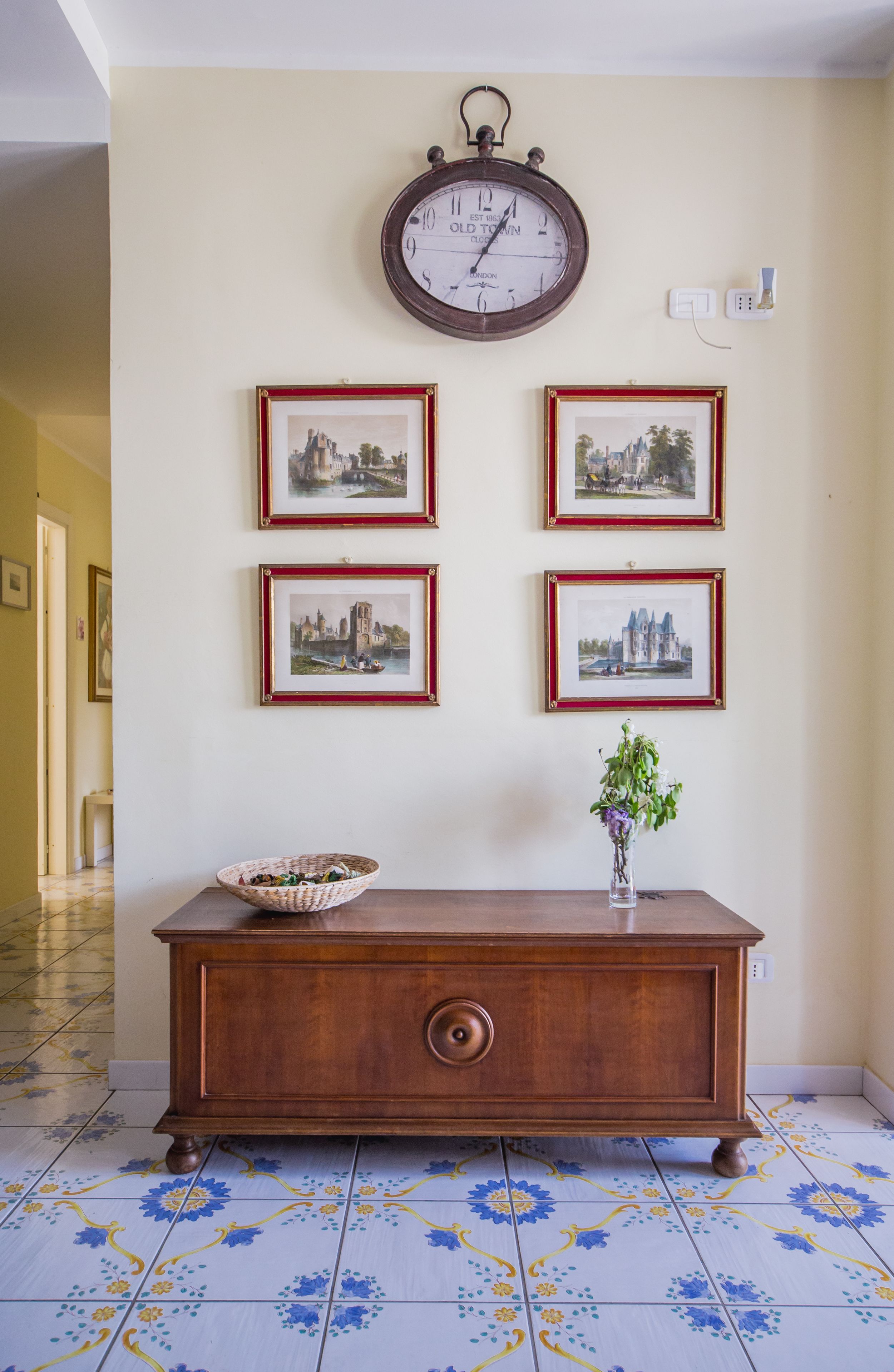 A wooden console table with a vase of flowers, a clock, and framed pictures on the wall.
