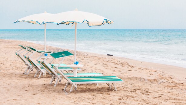A beach with white umbrellas and green and white striped lounge chairs. - Hotel Villa Maredona (Ascea)