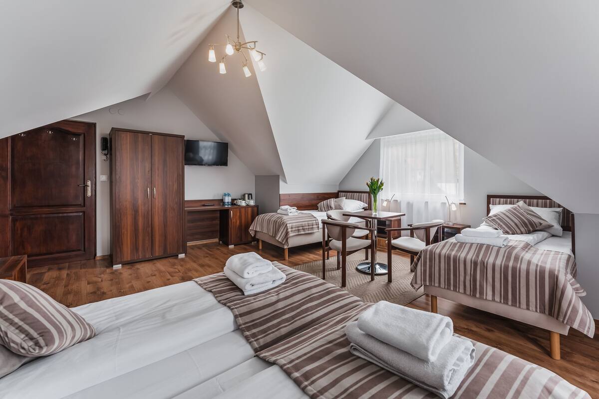 Ein modernes, helles Schlafzimmer im Dachgeschoss mit zwei Betten, einem Schreibtisch und einem Fernseher.