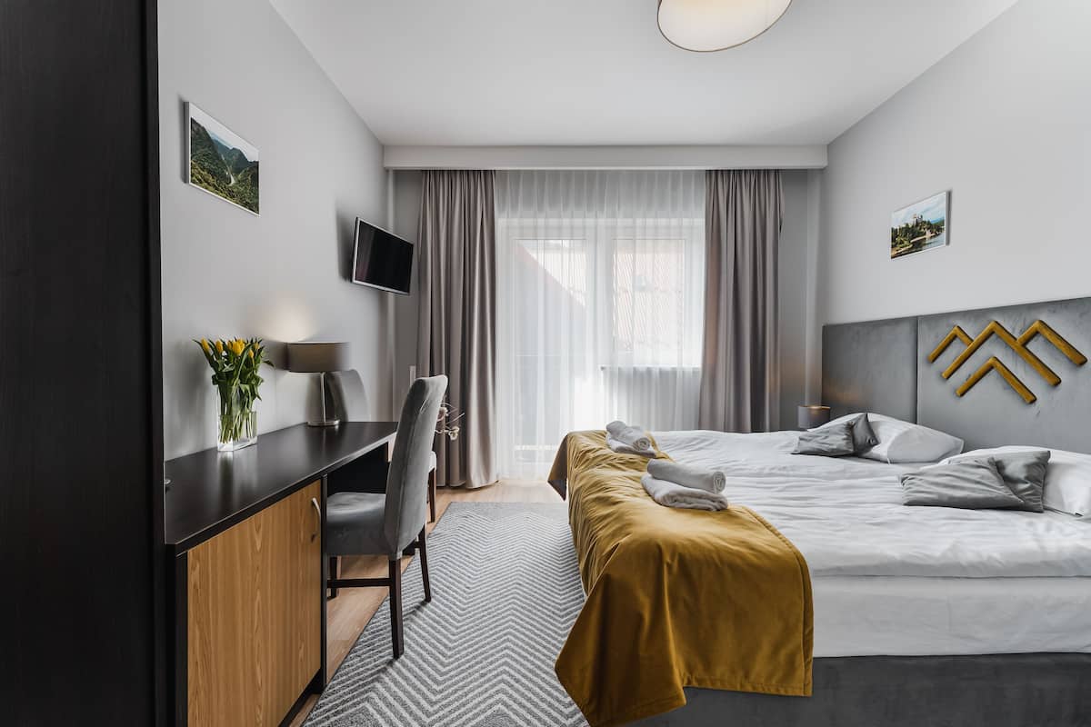 Ein modernes Hotelzimmer mit Bett, Schreibtisch, Stuhl und Fernseher.