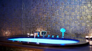 A bathroom with a blue-lit jacuzzi, a digital control panel, and a water feature.