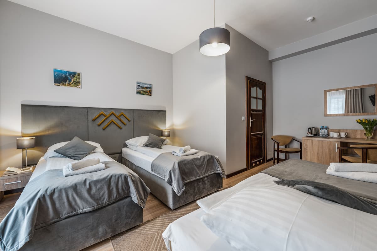 Ein Hotelzimmer mit zwei Betten, einem Schreibtisch, einem Stuhl und einer kleinen Küchenzeile.