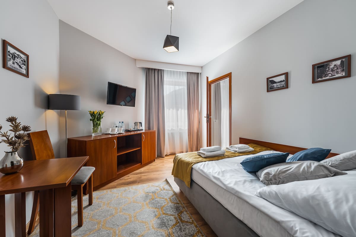 Ein modernes Hotelzimmer mit Bett, Nachttisch, Lampe, Fernseher und Schreibtisch mit Stuhl.