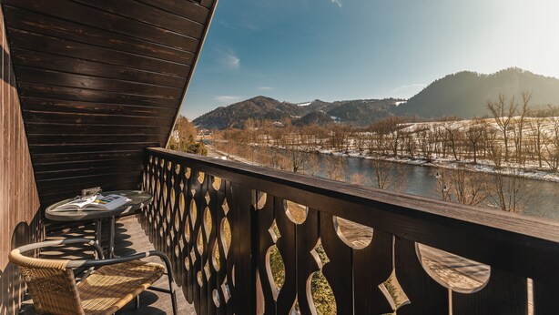 A wooden balcony with a view of a river and mountains.