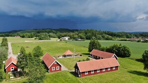 A rural landscape with red-roofed farm buildings, green fields, and a cloudy sky. - Vindängs Gård (Sloinge)