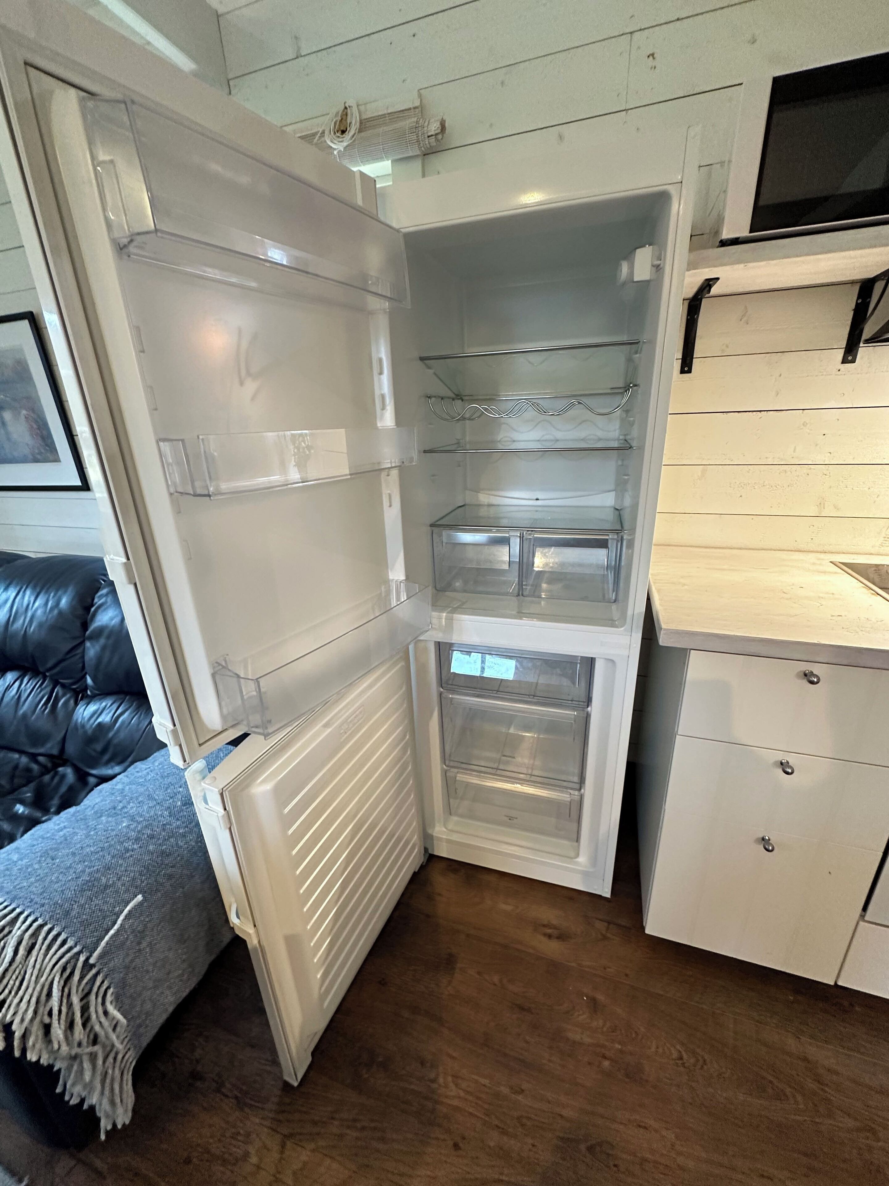 Een compacte keuken met een inbouwkoelkast, een houten aanrecht en een grijze bank.