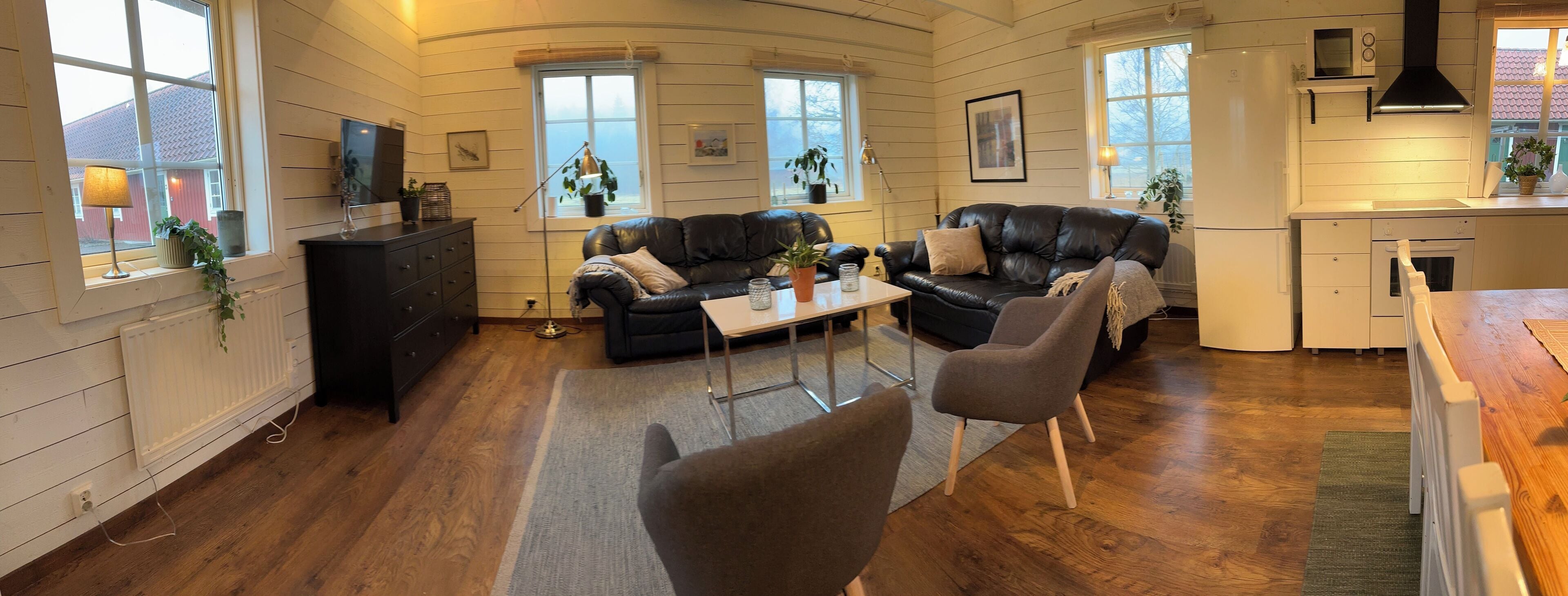 Ett mysigt vardagsrum med en öppen spis, en matplats och ett kök med vita köksluckor.