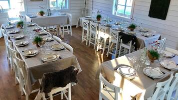 A dining area with multiple tables set for a meal, white chairs, and a rustic wooden floor.