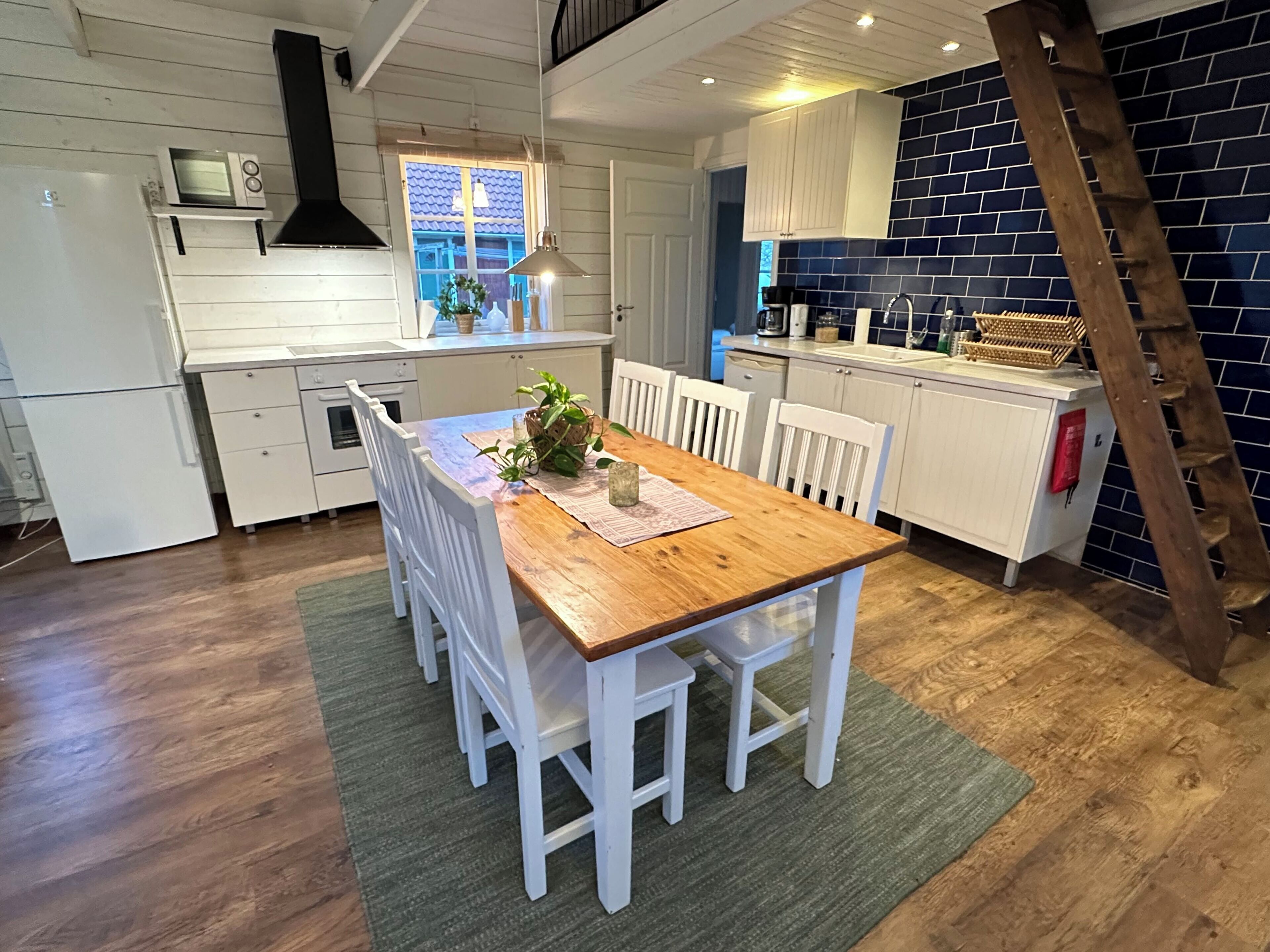 A compact kitchen with white cabinetry, a wooden dining table, and a green rug.