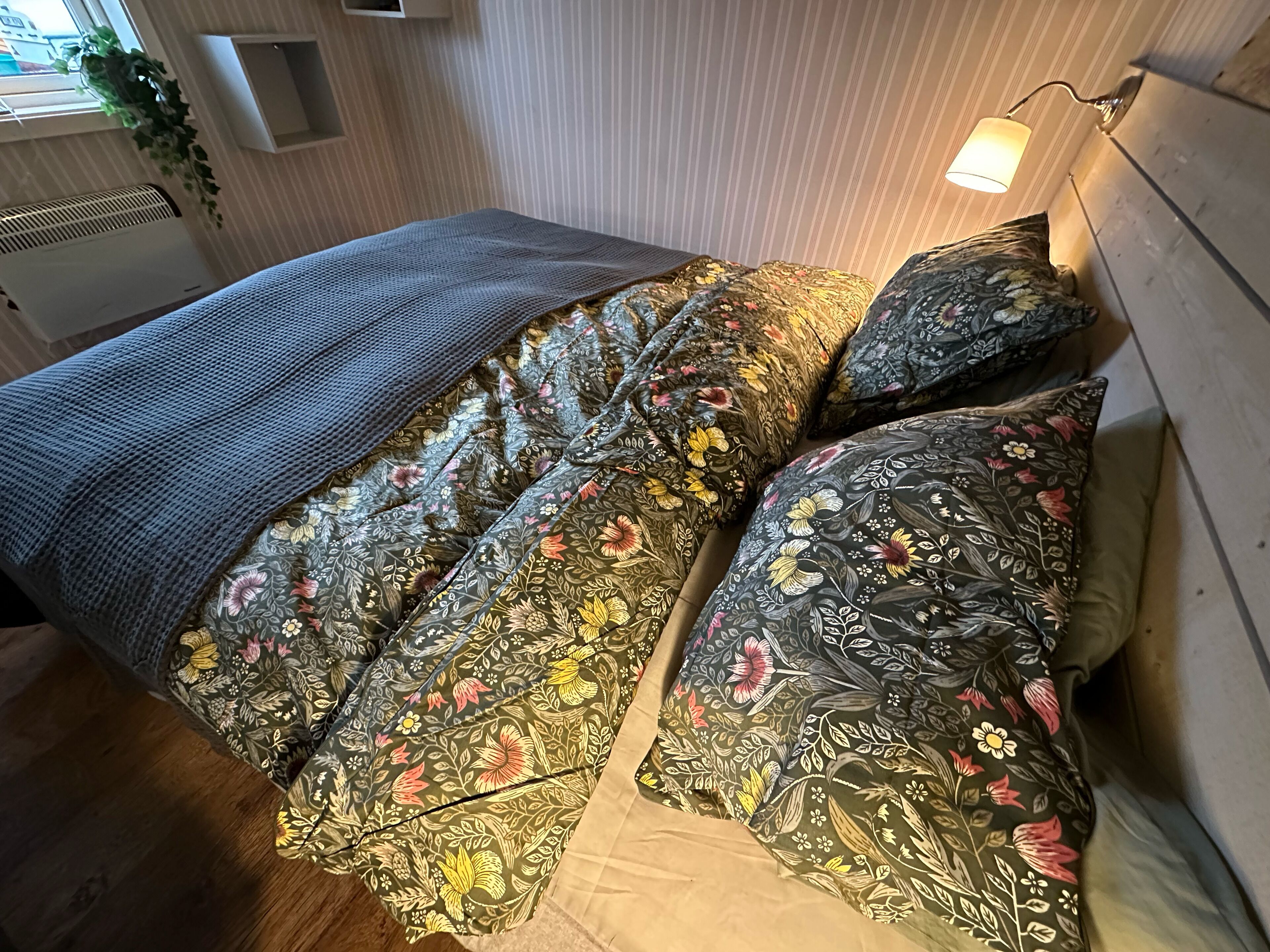 Un llit amb roba de llit de motius florals i una manta gris.