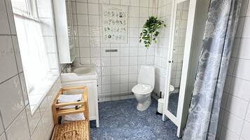 A bathroom with a white tiled floor, a white toilet, a sink, a mirror, and a window.