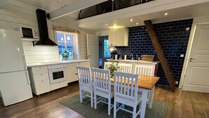 A kitchen with white cabinetry, a wooden dining table with white chairs, and a dark blue tiled backsplash. - Vindängs Gård (Sloinge)