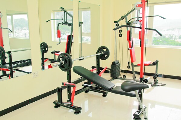 Une salle de sport équipée de matériel de musculation, d’un banc et d’un miroir qui reflète le matériel et les fenêtres.