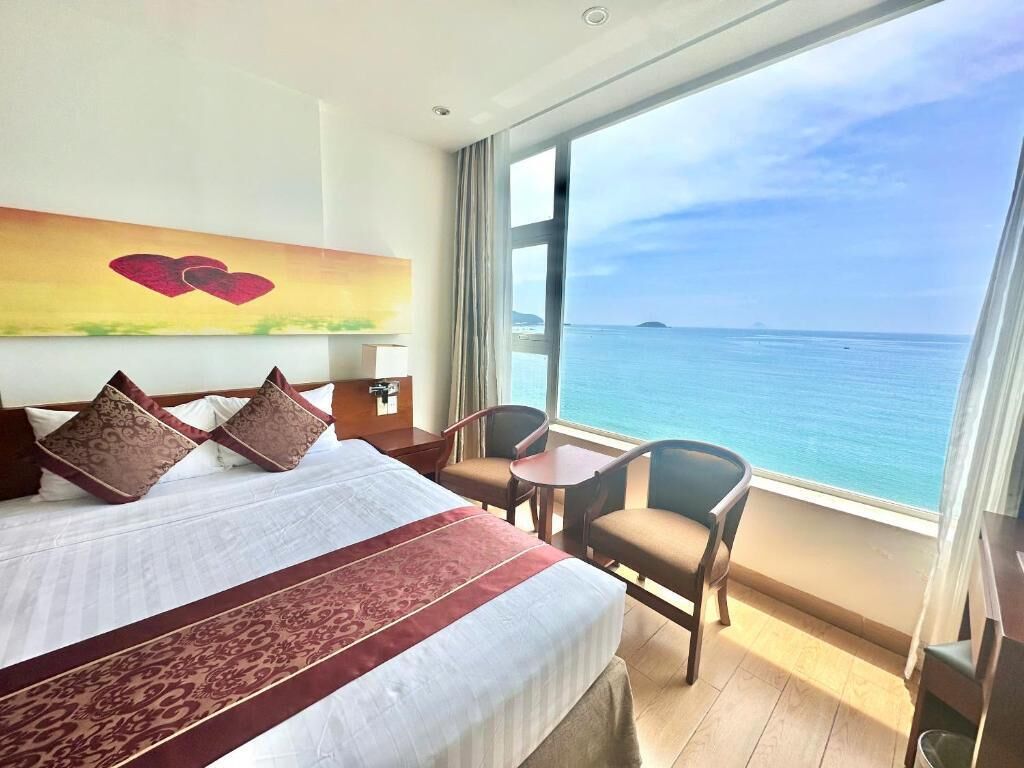 A hotel room with a large bed, a small table, two chairs, and a view of the ocean.