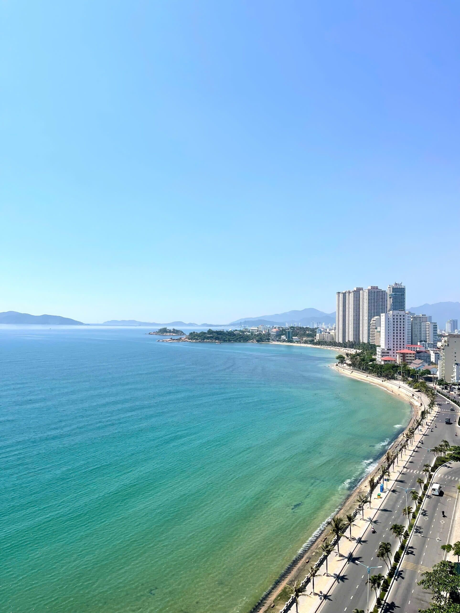 A coastal cityscape with a clear view of the ocean, a beach, and high-rise buildings.