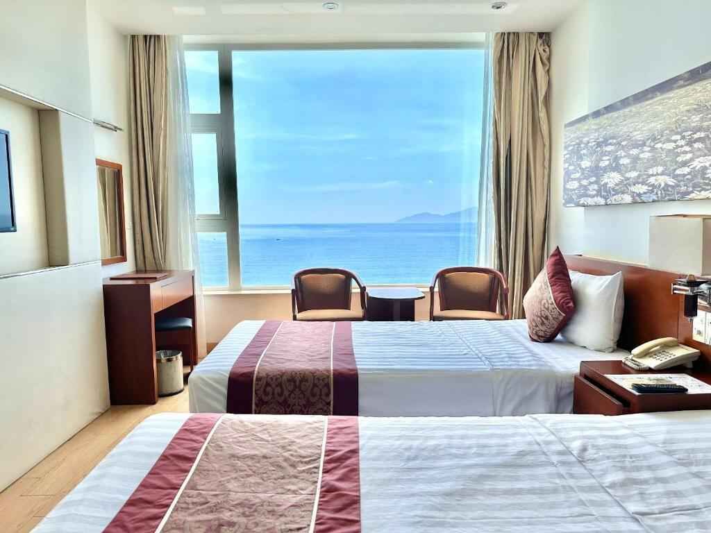 Una habitación de hotel con un ventanal grande, dos camas, un escritorio y una silla.