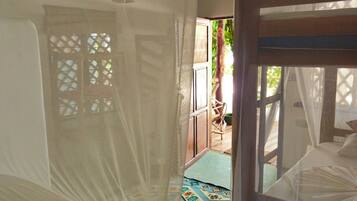 A room with a bed covered in white netting, a wooden bench, and a patterned rug on the floor.