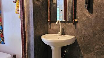 Un baño con lavamanos pedestal blanco, un espejo y ventana con vista a follaje.