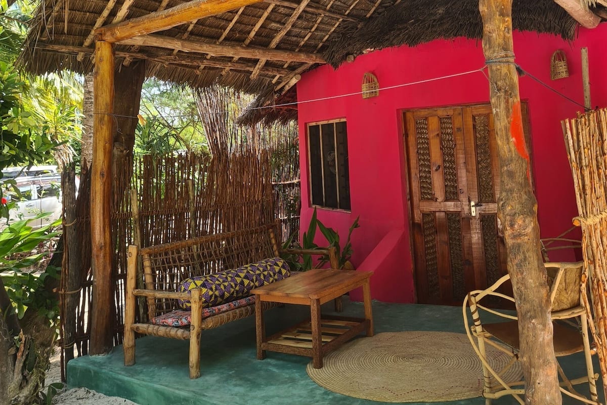 A rustic hut with a thatched roof, a wooden bench, and a woven chair.
