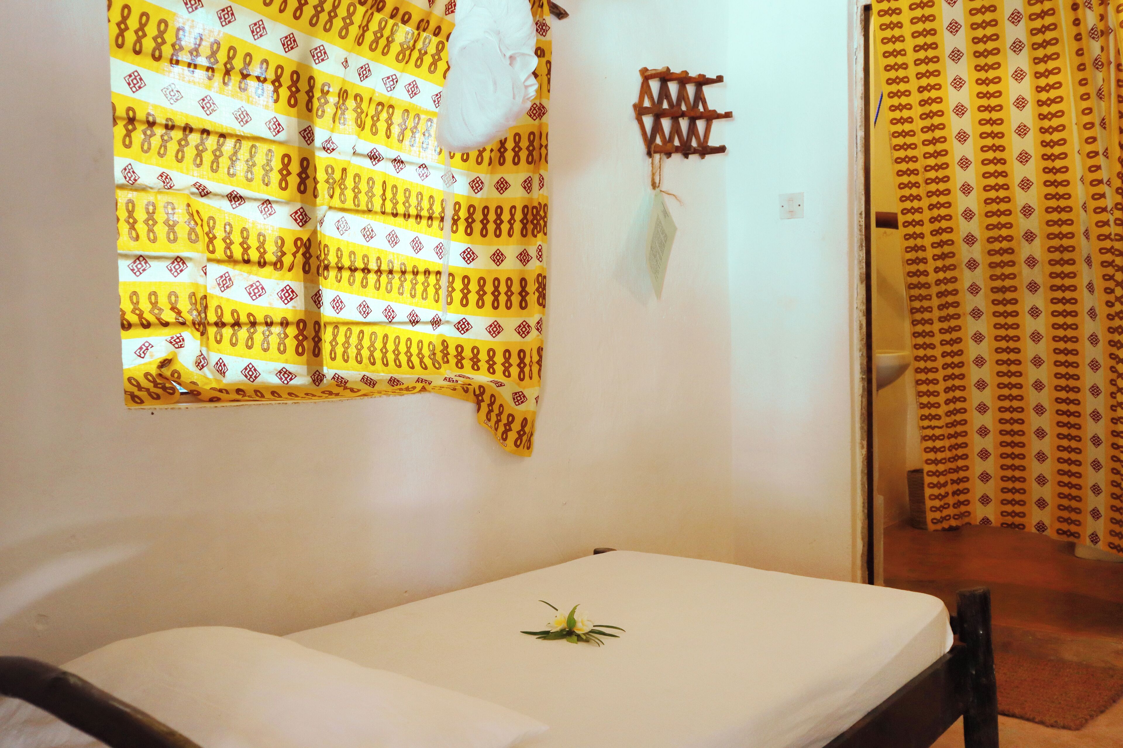 A room with a bed, a window with a yellow patterned curtain, and a wall-mounted decorative item.