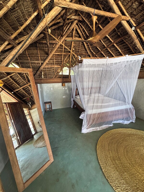 A room with a thatched roof, a bed with a mosquito net, and a woven mat on the floor. - Evergreen Bungalows (Bwejuu)