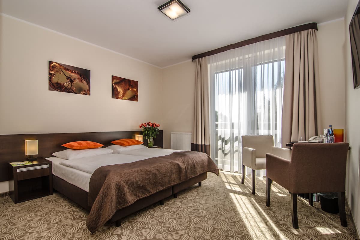 A hotel room with a large bed, a desk, a chair, and two paintings on the wall.