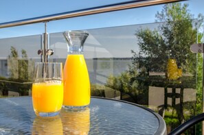 Two glasses of orange juice on a glass table with a metal railing in the background. - Hotel Emocja SPA (Mielno)