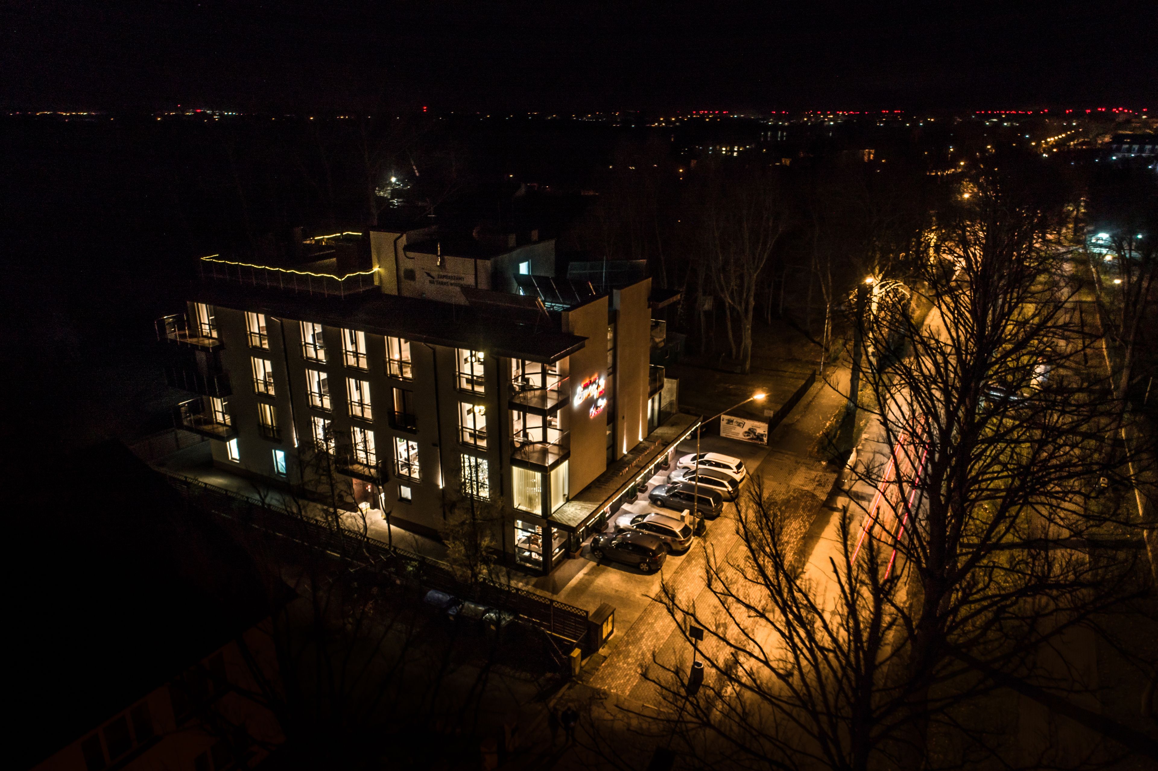 A multi-story building with illuminated windows and a parking area.
