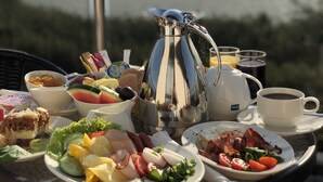 A table set with breakfast items including eggs, bacon, and fruit, with a view of a lake in the background. - Hotel Emocja SPA (Mielno)