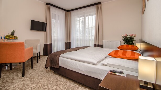 A hotel room with a bed, a desk, a chair, a TV, and a window with curtains. - Hotel Emocja SPA (Mielno)